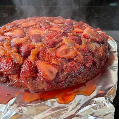 A freshly inverted strawberry upside-down cake with juices and caramel pouring down the sides