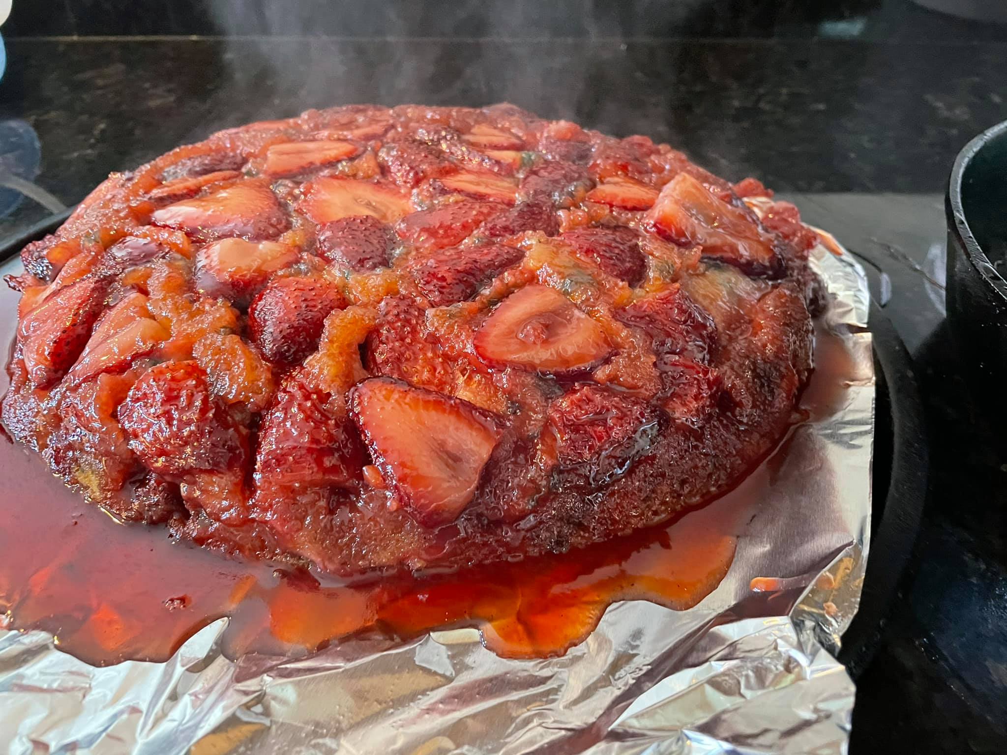 A freshly inverted strawberry upside-down cake with juices and caramel pouring down the sides