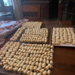 dozens of baked clothespin cookie shells cooling on wire racks on a large wooden table