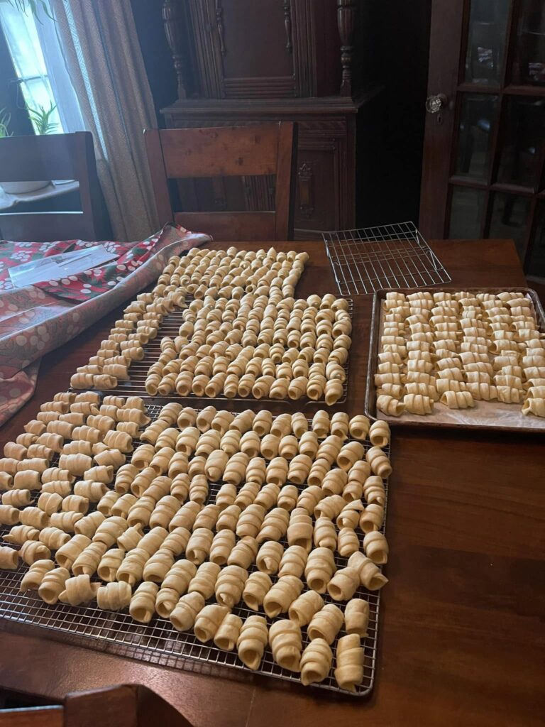 dozens of baked clothespin cookie shells cooling on wire racks on a large wooden table