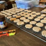 dozens of soft peanut butter cookies cooling on racks with sugar sparkle, surrounded by peanut butter and chocolate ingredients