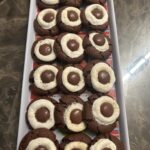 chocolate cocoa bomb cookies arranged neatly on a tray, each topped with a melted marshmallow and Hershey Drop