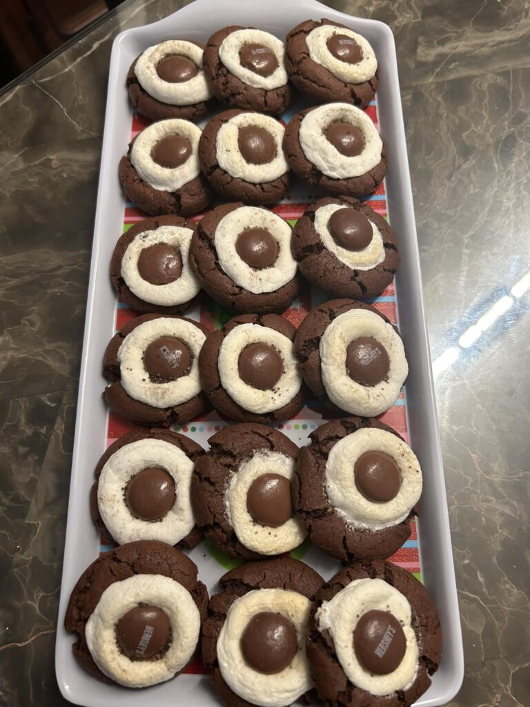 chocolate cocoa bomb cookies arranged neatly on a tray, each topped with a melted marshmallow and Hershey Drop