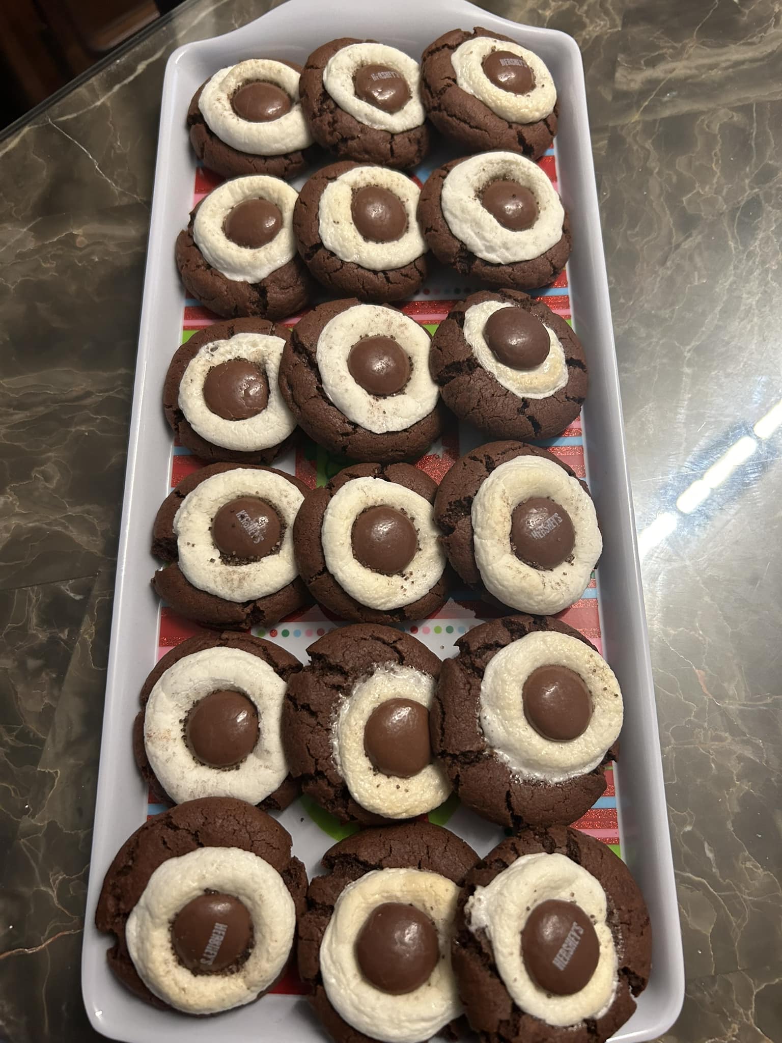 chocolate cocoa bomb cookies arranged neatly on a tray, each topped with a melted marshmallow and Hershey Drop