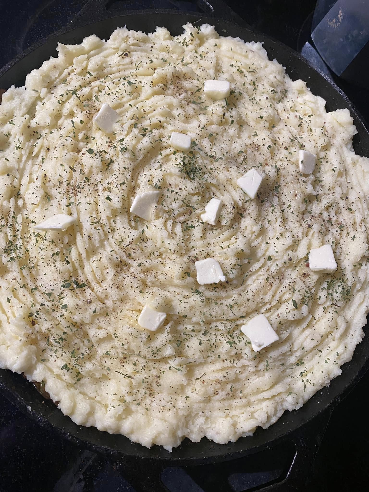 mashed potatoes spread over cottage pie filling in cast iron skillet before baking