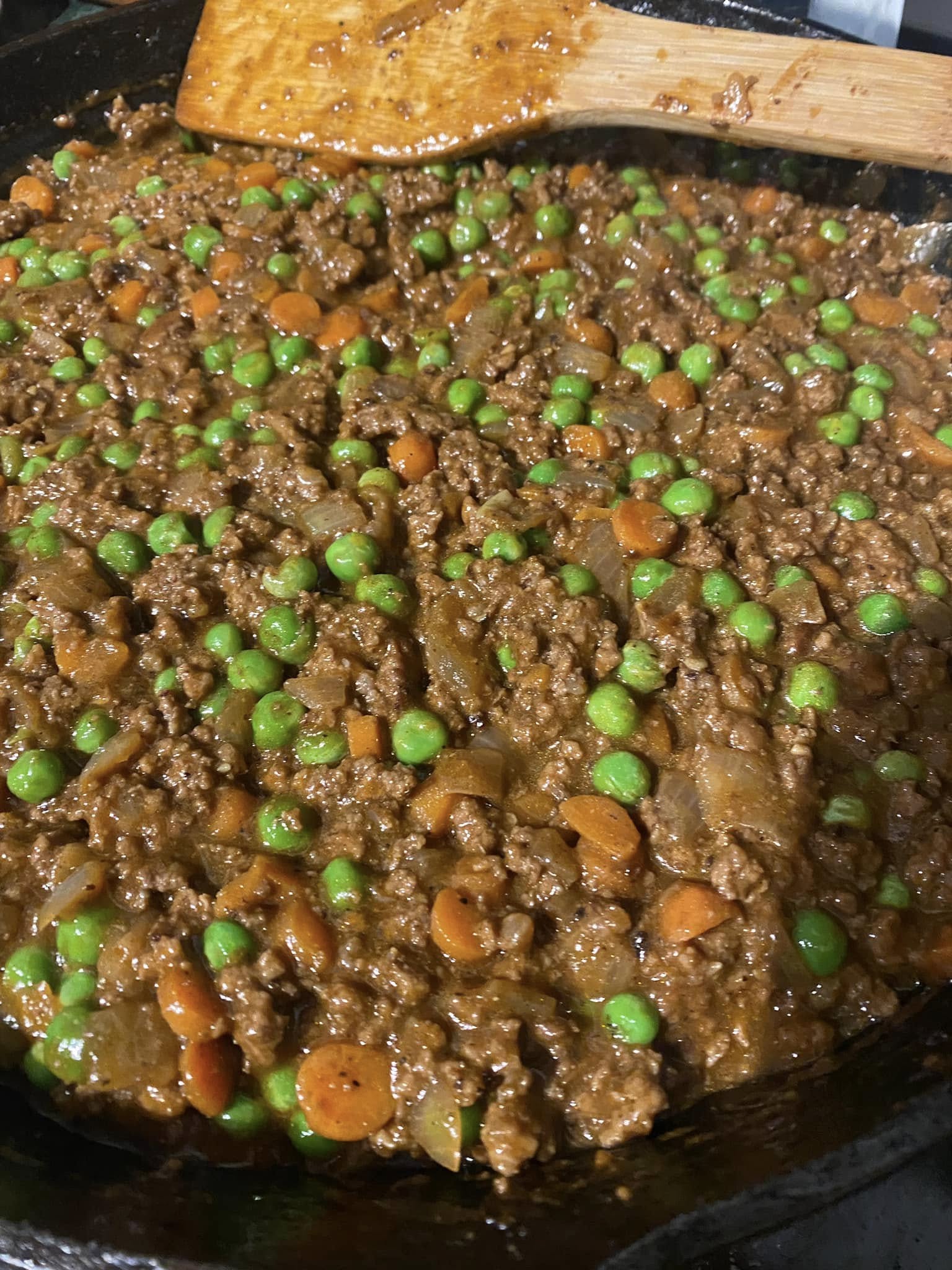 browned ground beef filling thickening in cast iron skillet with peas added