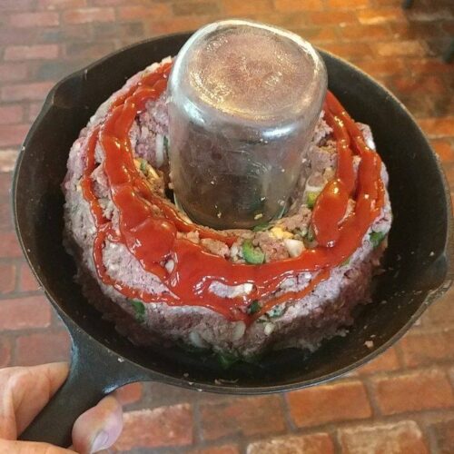 Raw meatloaf shaped around a jar in cast iron skillet, topped with Sriracha ketchup