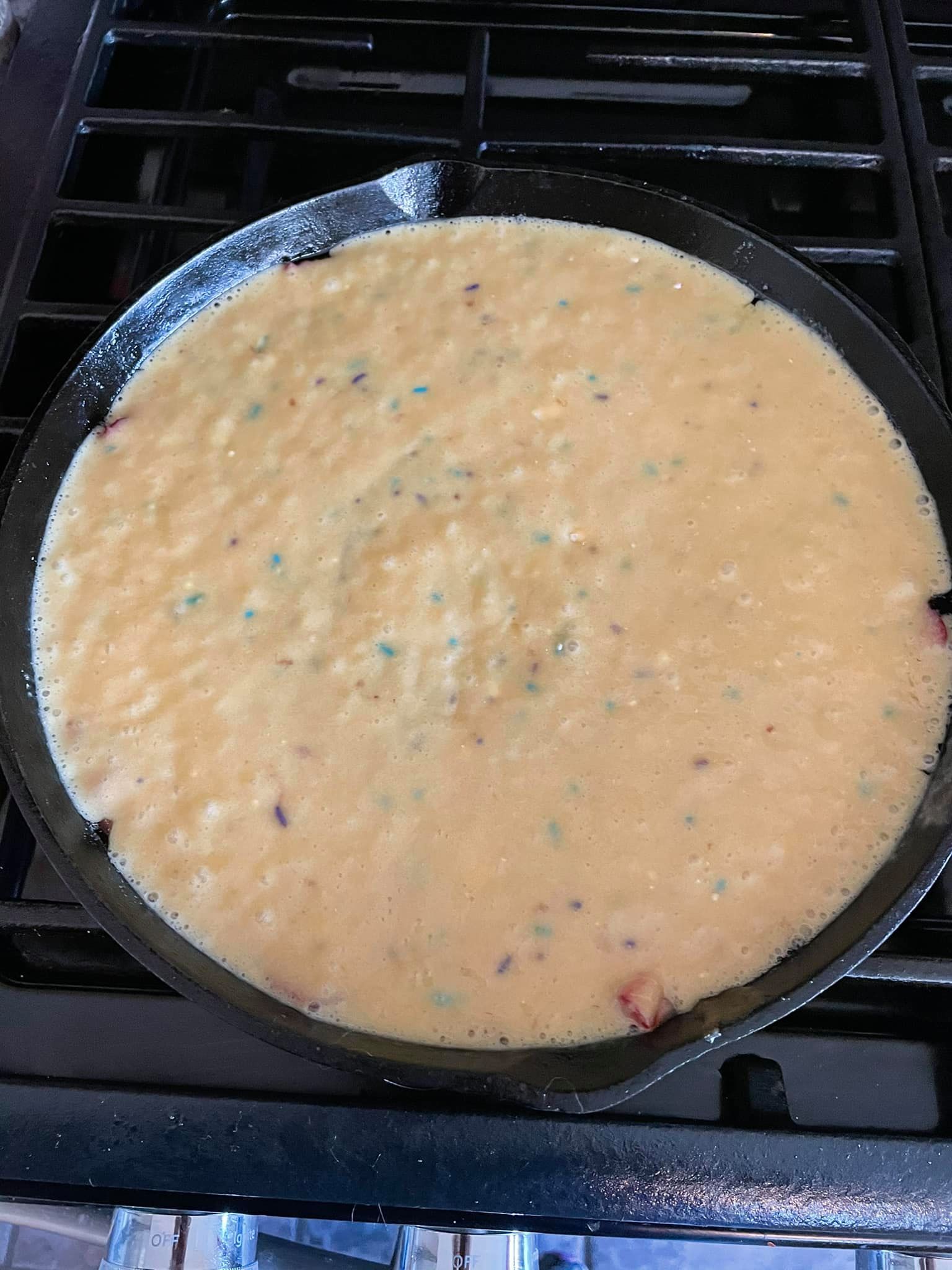 Smooth cake batter poured over strawberries in a cast iron skillet before baking.