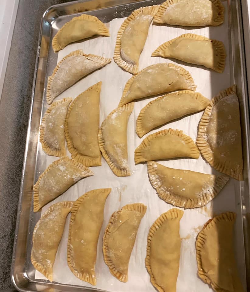 unbaked hand pies arranged on a tray, edges crimped and dusted with flour
