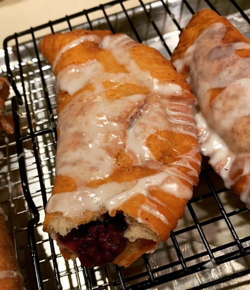 fried pie with apple filling inside, surrounded by other glazed pies on cooling rack
