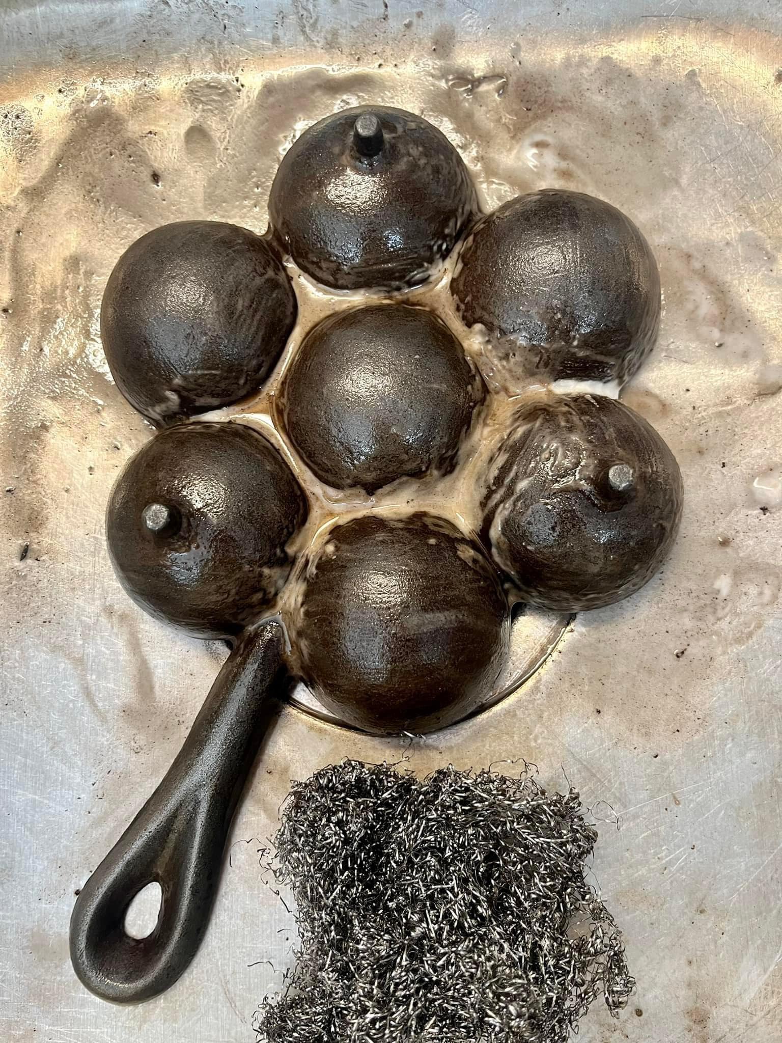 Close-up of hand scrubbing rust off cast iron with steel wool and baking soda