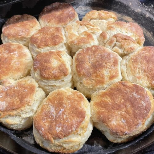 golden brown homemade buttermilk biscuits baked in a cast iron skillet, stacked together with flaky layers visible