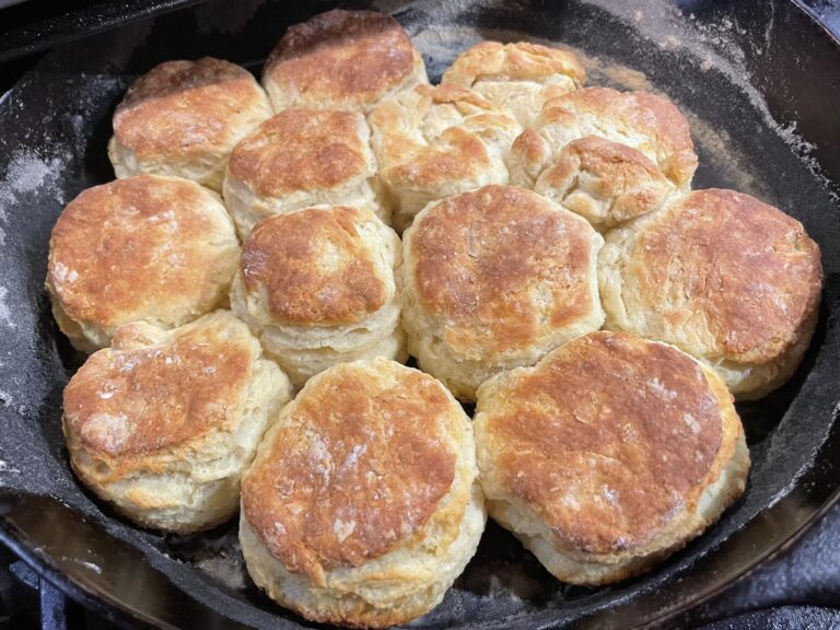 golden brown homemade buttermilk biscuits baked in a cast iron skillet, stacked together with flaky layers visible