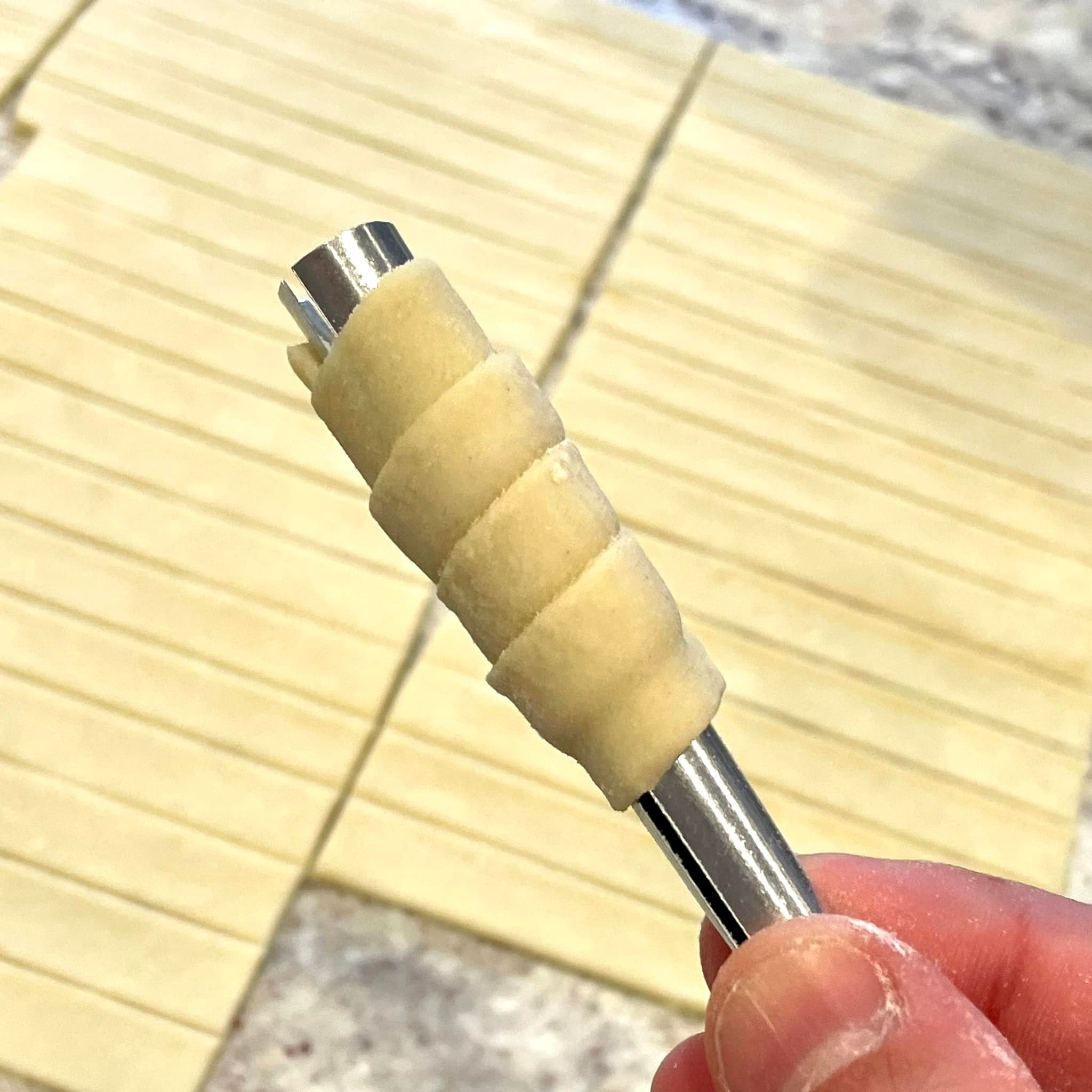 hand holding a wrapped clothespin cookie form with dough spiraled around it