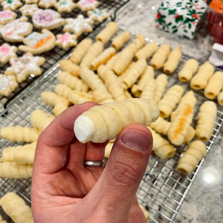 hand holding a finished lady lock cookie filled with creamy frosting