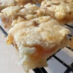 gooey apricot shortbread bar with buttery crumb topping cooling on rack