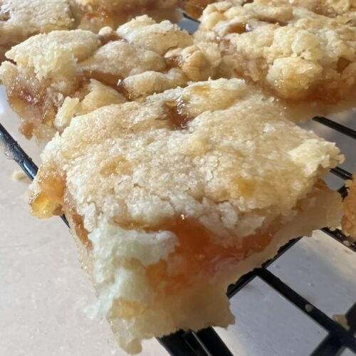 gooey apricot shortbread bar with buttery crumb topping cooling on rack
