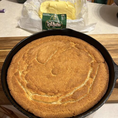 freshly baked southern buttermilk cornbread in black cast iron skillet with butter in background]
