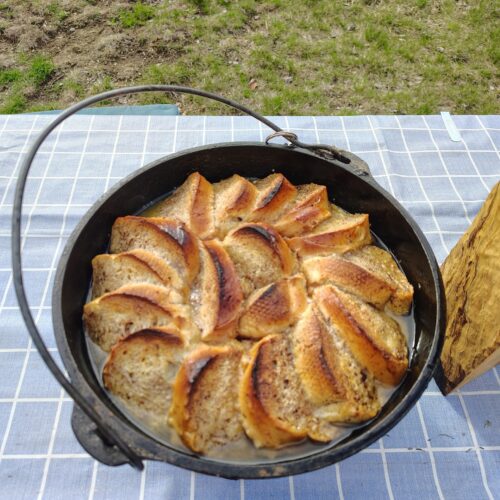 cooked Dutch oven peach French toast outdoors in a black cast iron Dutch oven with toasted bread slices arranged in a circular pattern