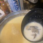 pot of creamy oyster stew with oysters floating in broth, saltines and hot sauce visible in the background