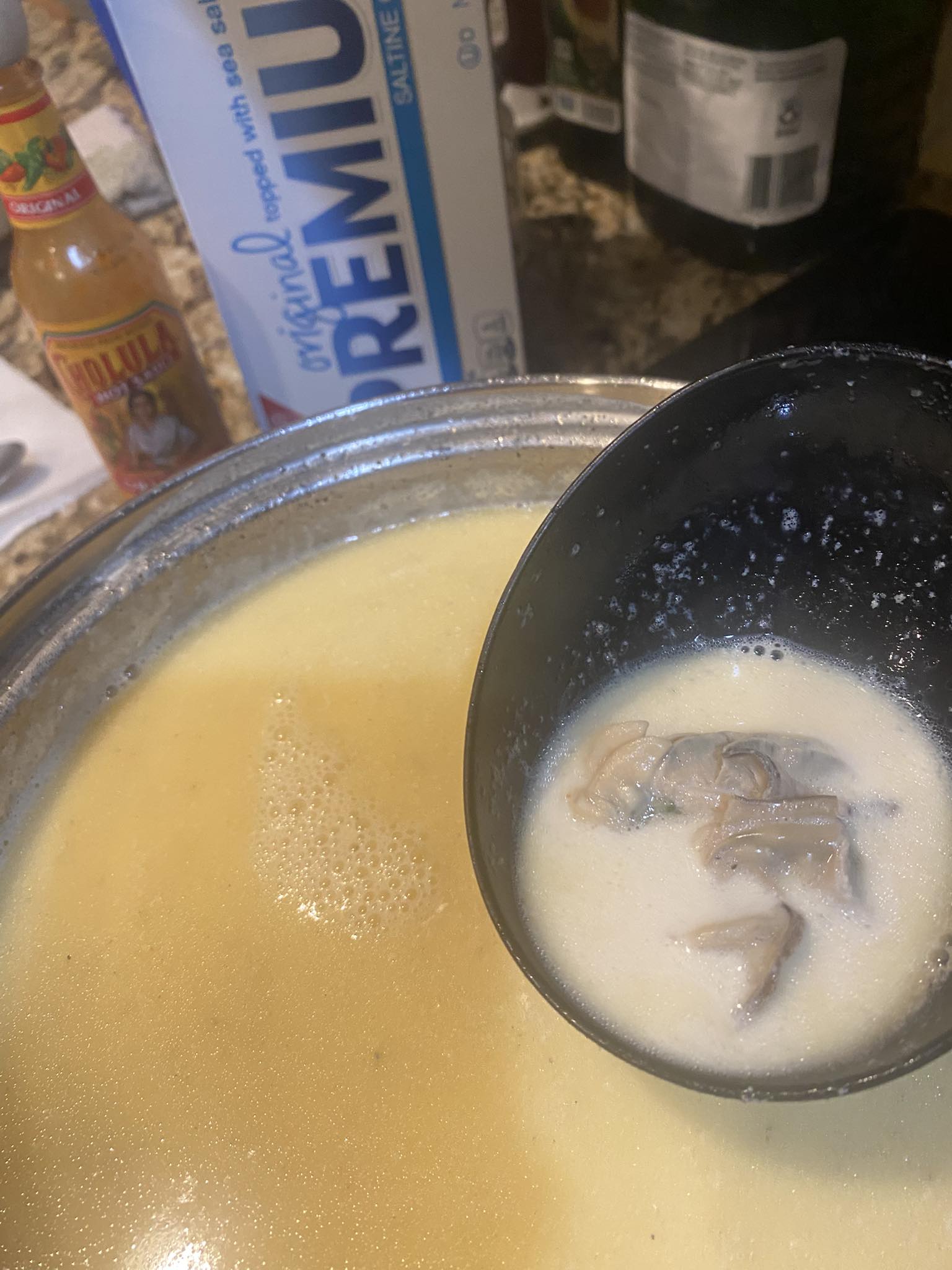 pot of creamy oyster stew with oysters floating in broth, saltines and hot sauce visible in the background