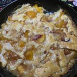 golden brown peach cobbler baked in a cast iron skillet with bubbling syrup and crisp edges