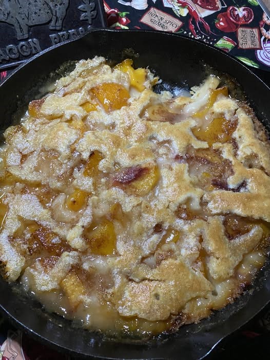 golden brown peach cobbler baked in a cast iron skillet with bubbling syrup and crisp edges