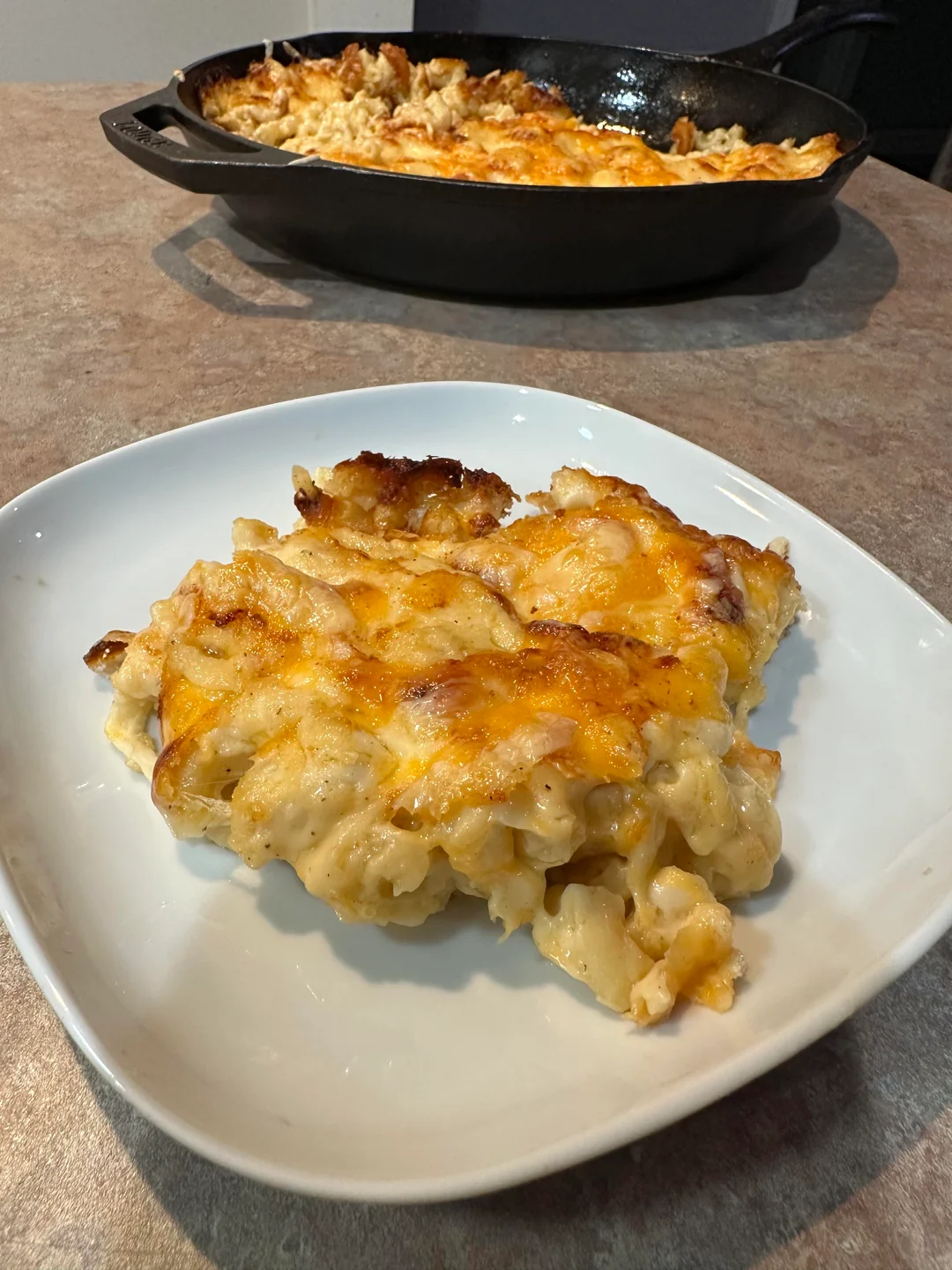 serving of cheesy baked mac and cheese on plate with skillet in background