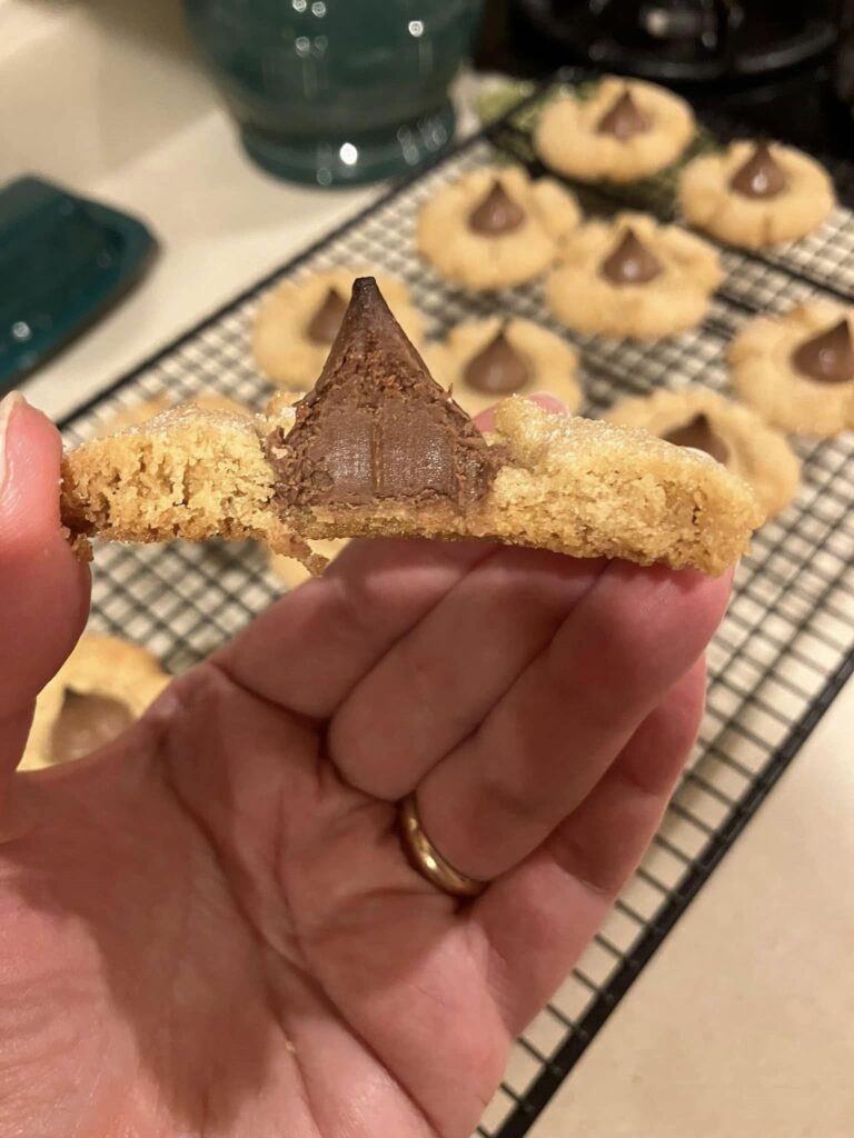 eanut butter blossom cookie broken in half showing soft, chewy texture and melted chocolate Kiss center