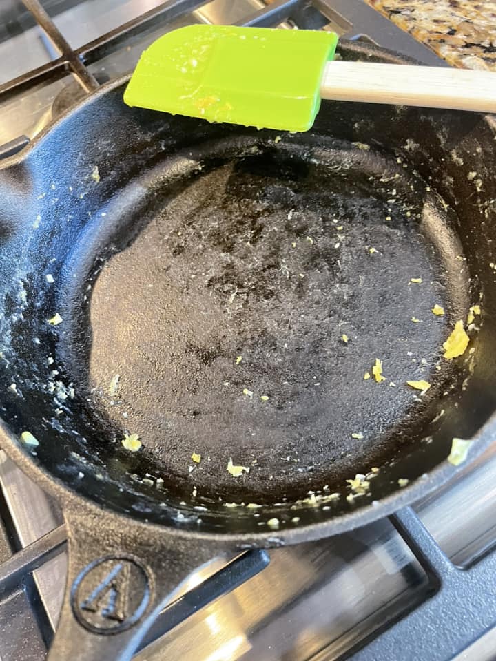 An empty cast iron skillet after cooking eggs, showing very minimal residue and crumbs, proving the non-stick technique worked