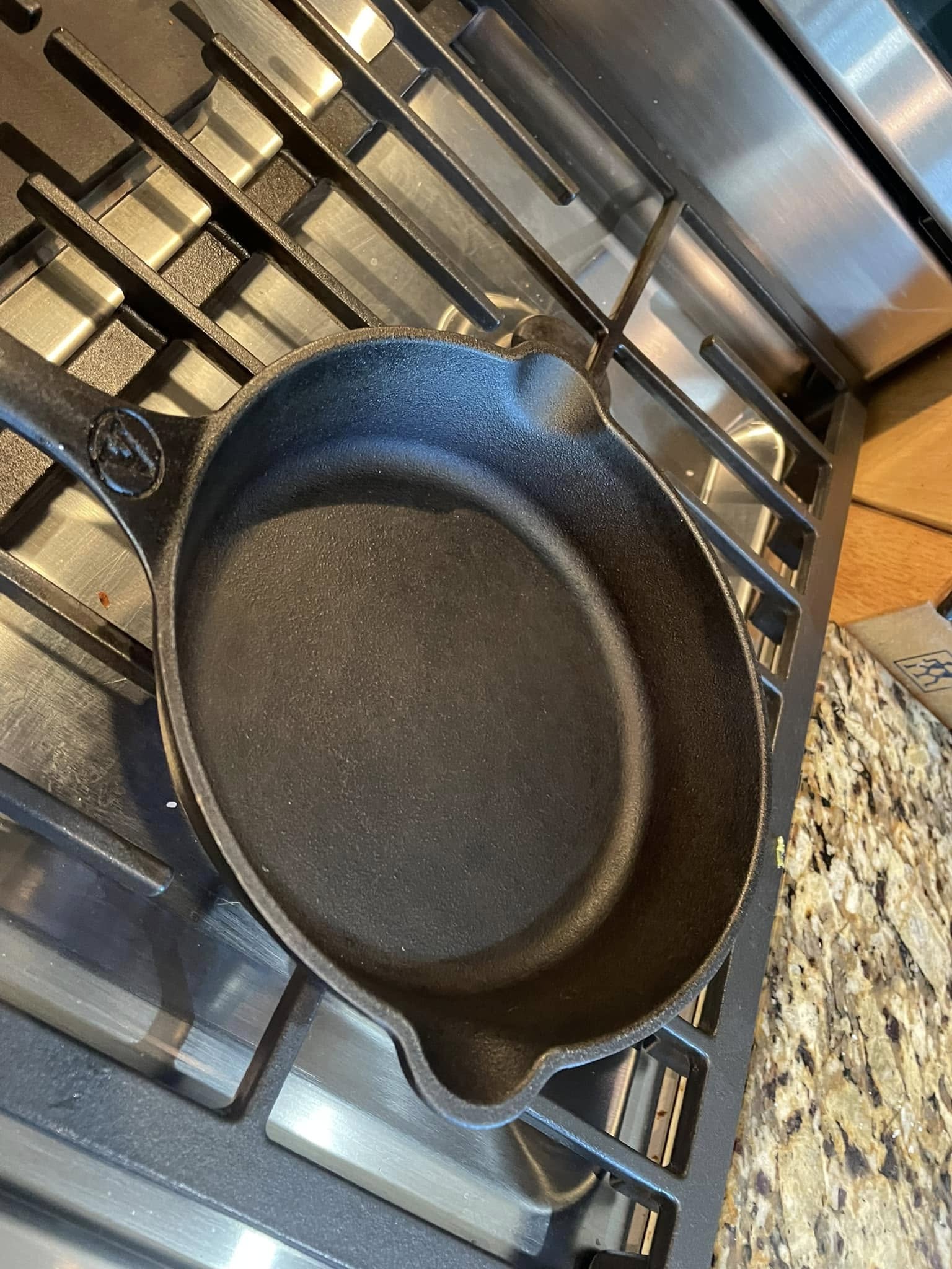 An empty, seasoned 8-inch Victoria cast iron skillet sitting on a gas stovetop burner, showing a smooth black interior