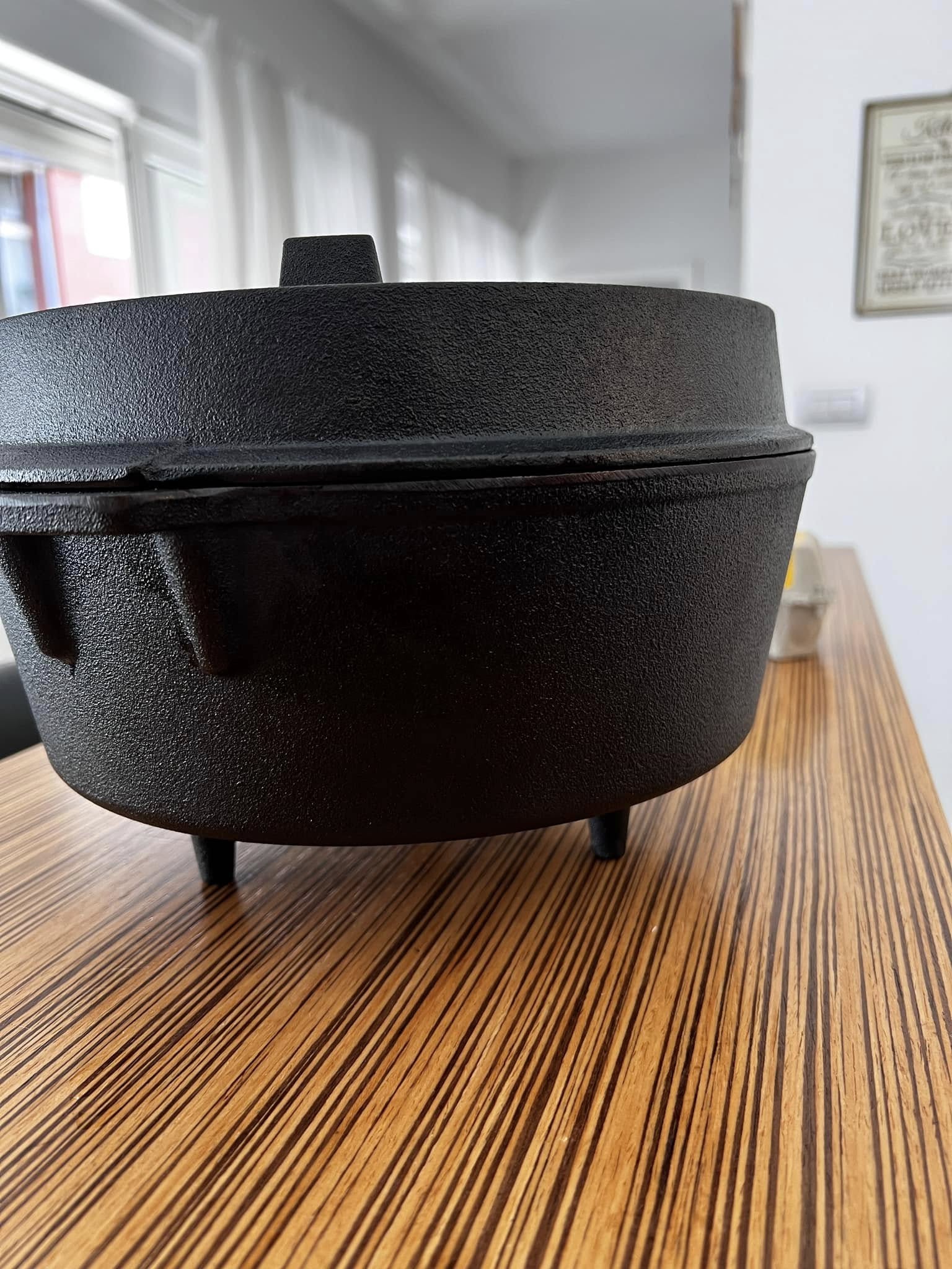 A side view of the restored Dutch oven sitting on a wooden table, showing the deep black color and clean surface free of rust.