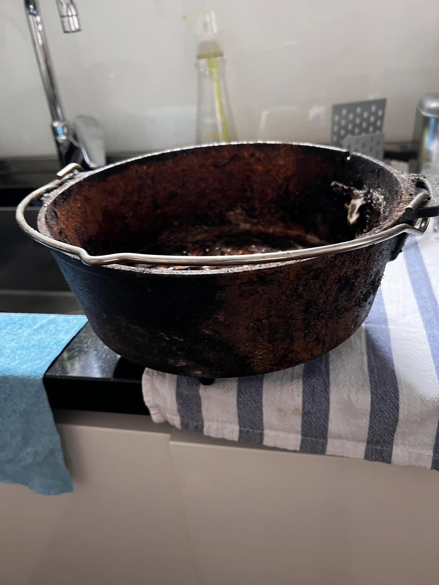 Side profile of the rusty Dutch oven sitting on a counter, showing the deep corrosion and discoloration on the exterior walls
