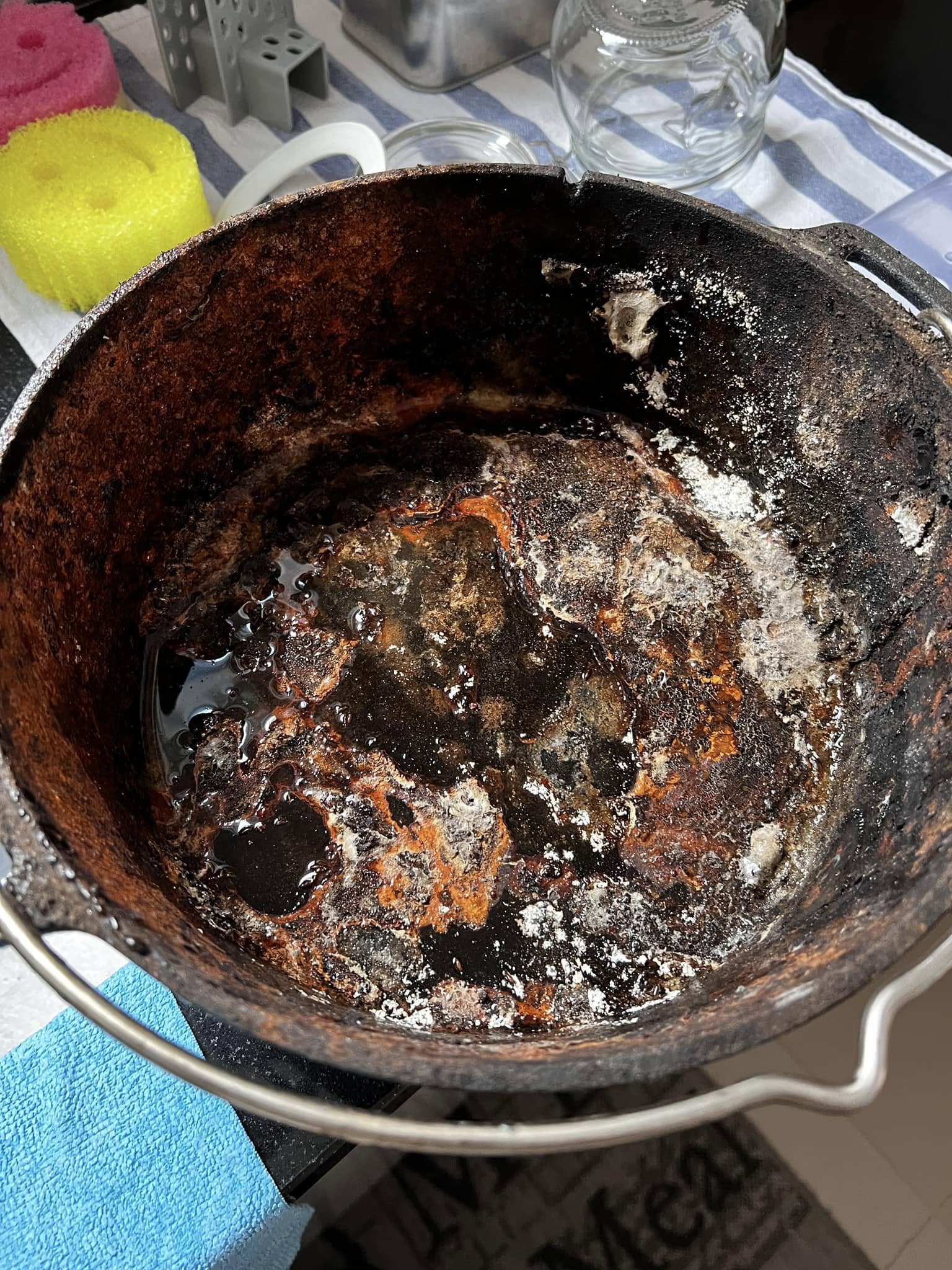 A top-down view of a severely rusted cast iron Dutch oven interior, showing dark water, orange rust flakes, and white mold spots.