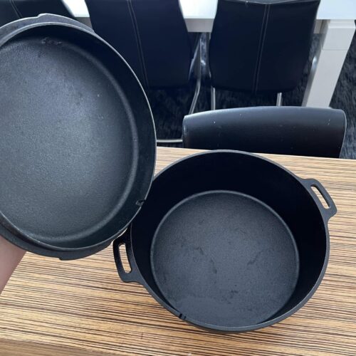 The fully restored cast iron Dutch oven with the lid held open, revealing a smooth, jet-black, seasoned interior.