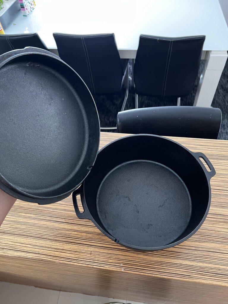 The fully restored cast iron Dutch oven with the lid held open, revealing a smooth, jet-black, seasoned interior.