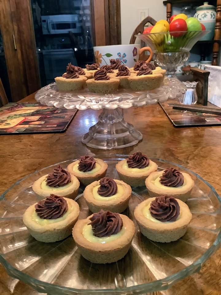 A crystal platter displaying Boston Cream Pie Cookie Cups, featuring golden cookie bases filled with yellow custard and topped with piped chocolate ganache rosettes.