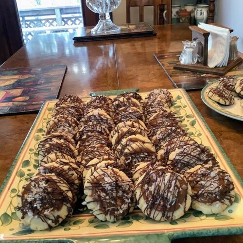 A large platter filled with dozens of homemade Samoa sugar cookies, showcasing the golden toasted coconut topping and zig-zag chocolate drizzle