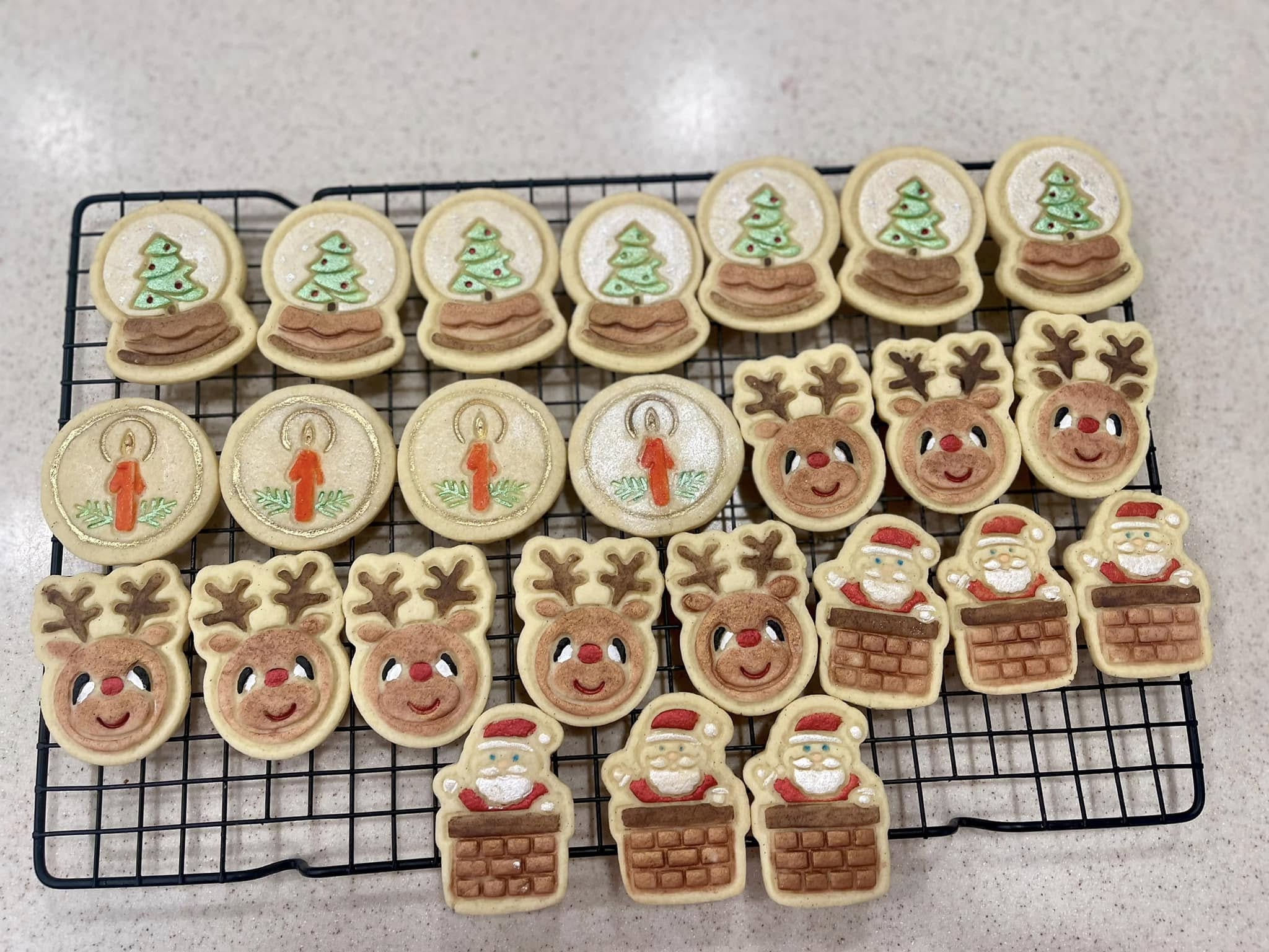 A wire rack filled with decorated Christmas cookies including smiling snowmen with red scarves, candy canes with gold bows, holly leaves with red berries, and colorful knit-texture mittens.