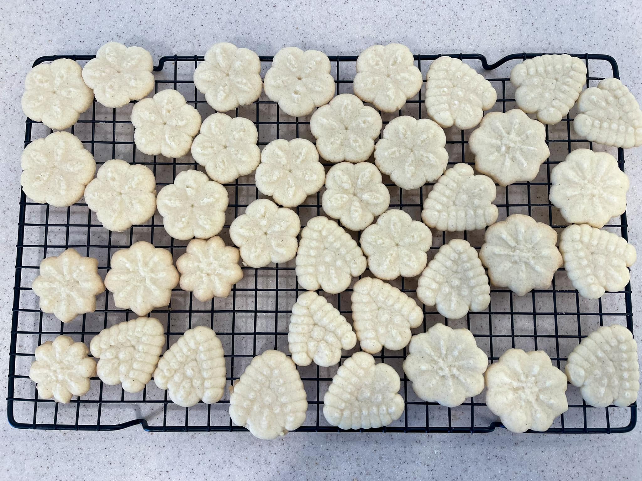 Golden baked Classic Butter Spritz Cookies in flower and leaf shapes cooling on a black wire rack