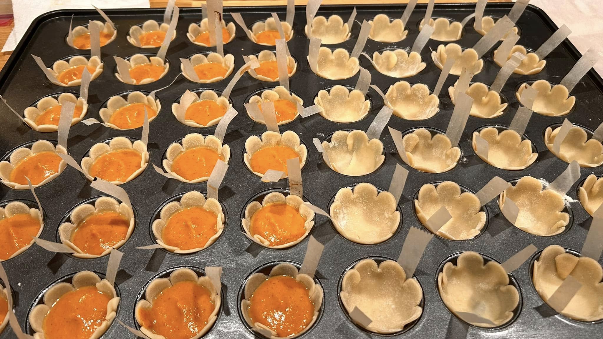 A mini muffin tin prepped for baking with narrow strips of parchment paper placed in each cavity under the dough shells to act as lifting handles