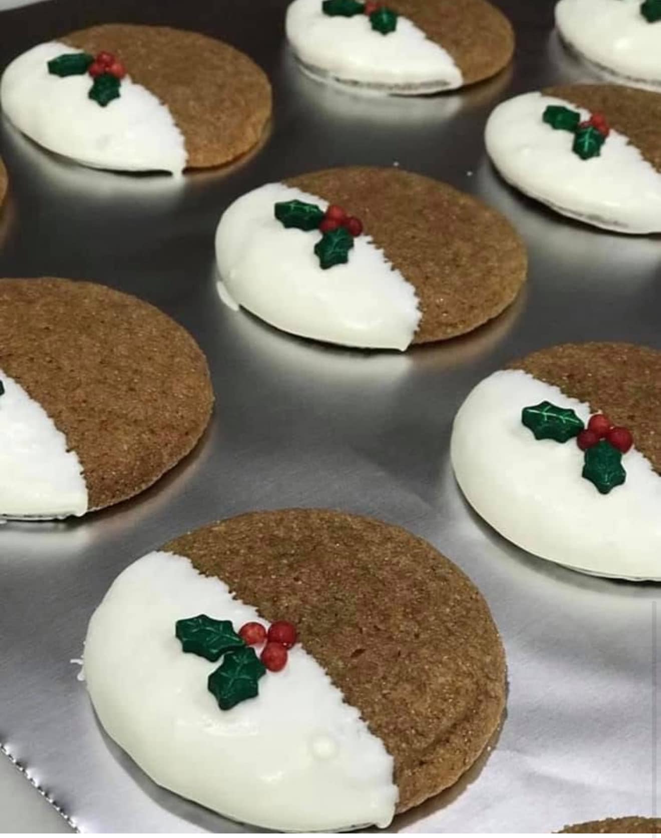 A baking sheet full of baked ginger cookies featuring a smooth white chocolate dip and holly decoration