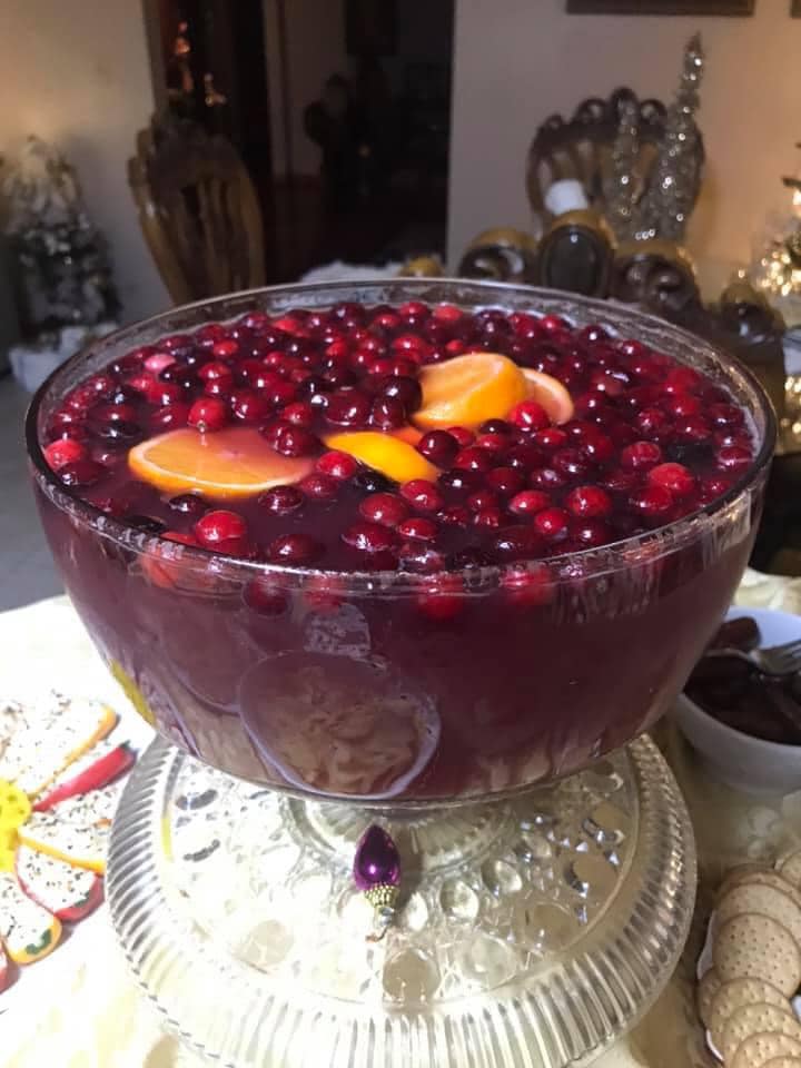 A crystal punch bowl filled with dark red Christmas punch, topped with floating orange slices and fresh cranberries