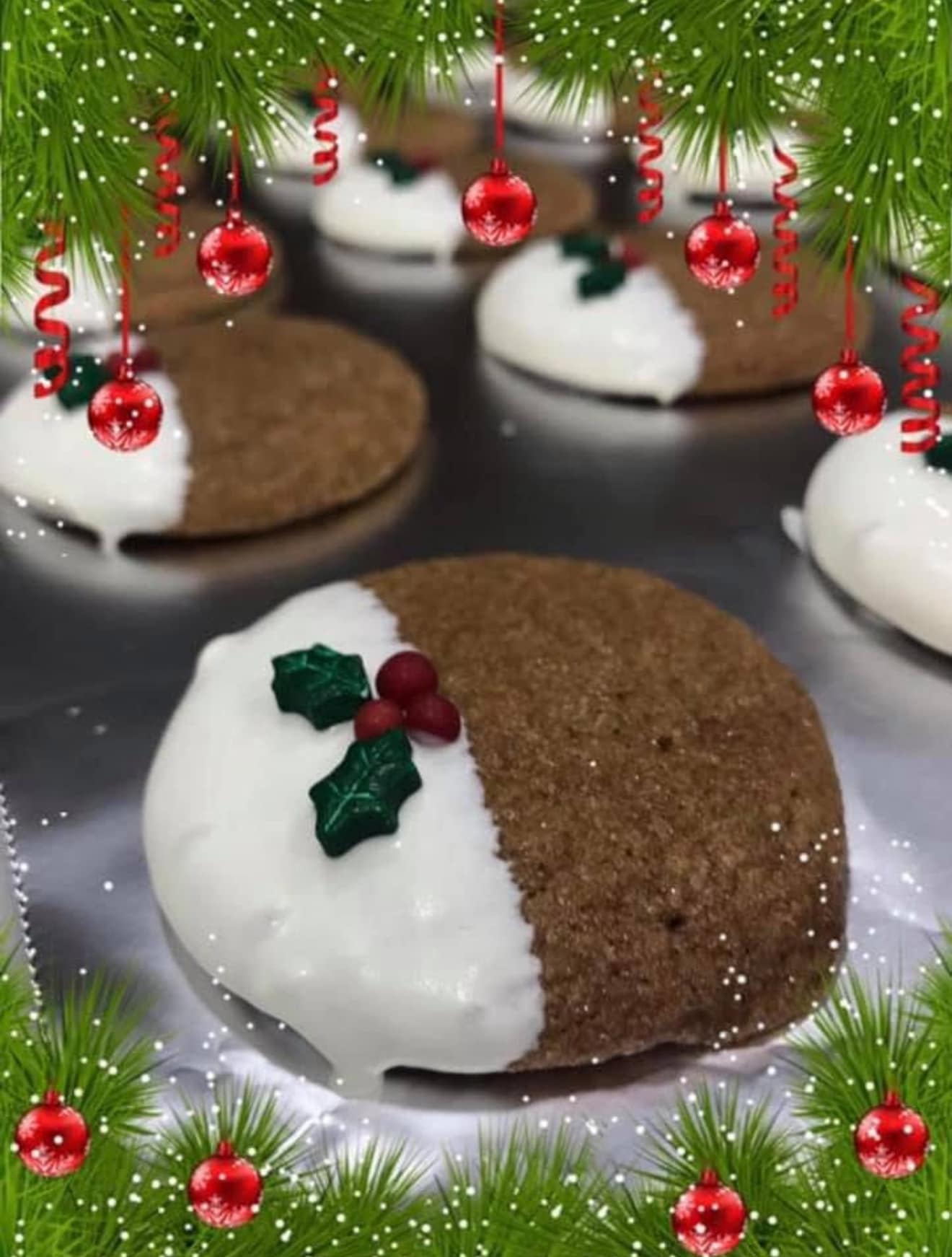A close-up of a soft ginger cookie dipped halfway in white chocolate, topped with green holly leaf and red berry sprinkles