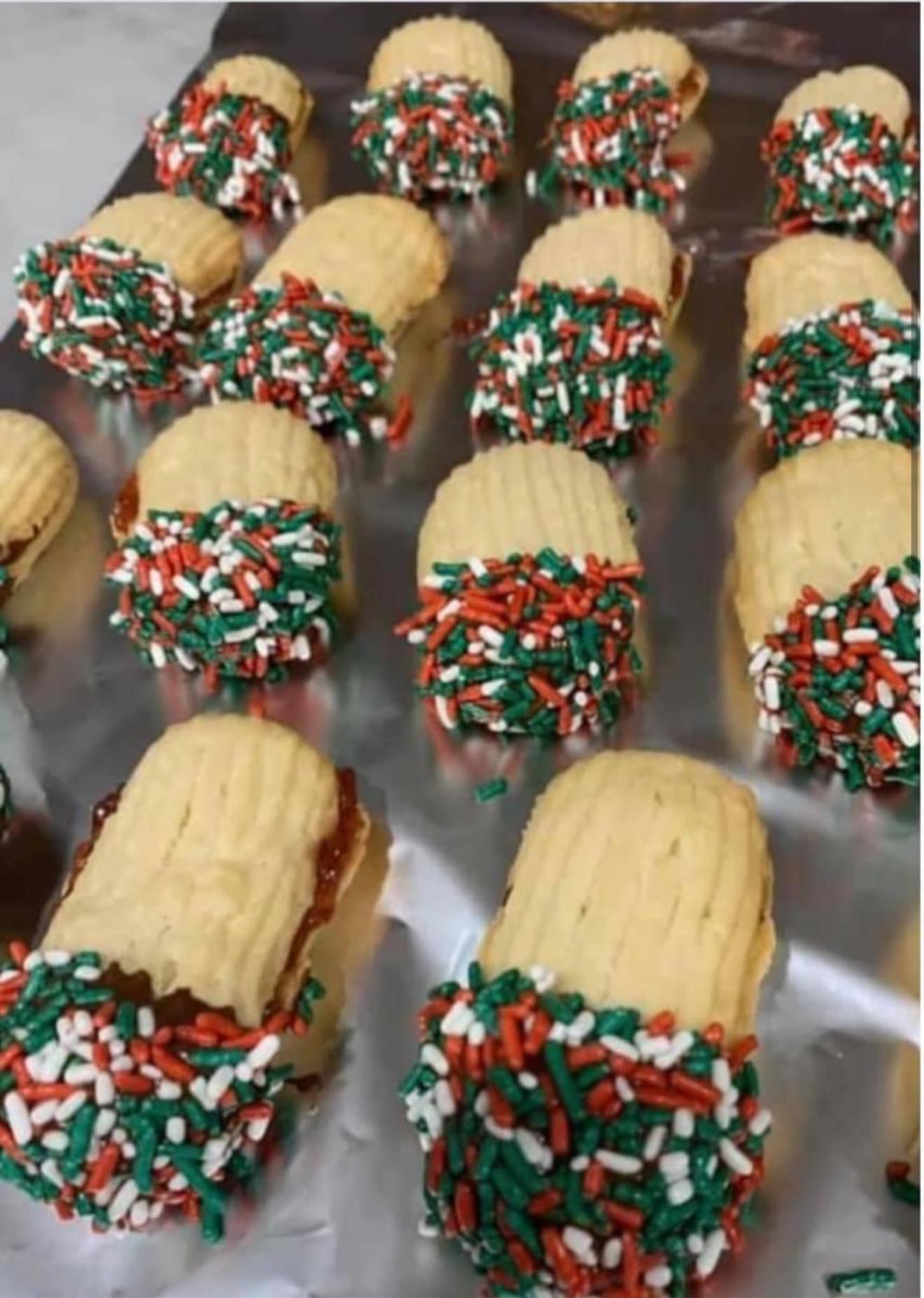 Rows of Jelly Stick Cookies sandwiched with jam and dipped in chocolate with Christmas sprinkles