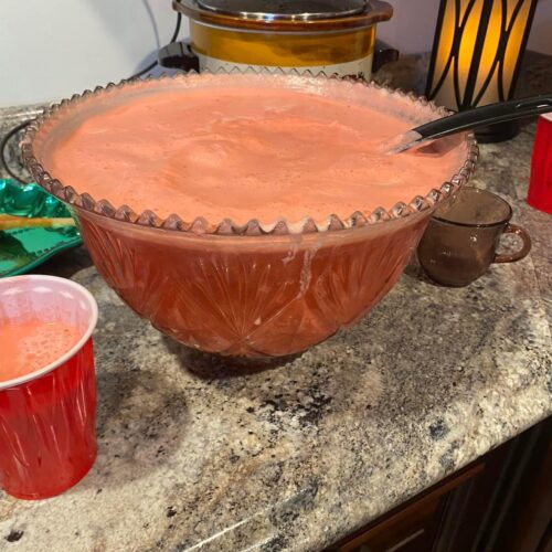 A large glass punch bowl filled with pink Christmas Sherbet Punch, showing a frothy creamy layer on top