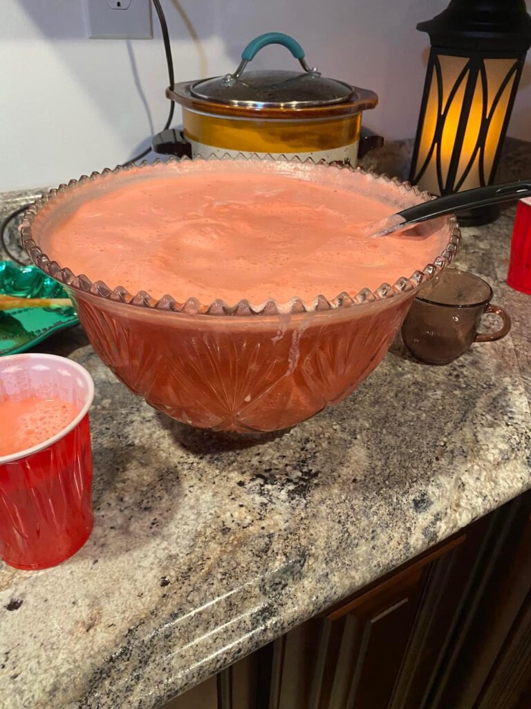 A large glass punch bowl filled with pink Christmas Sherbet Punch, showing a frothy creamy layer on top