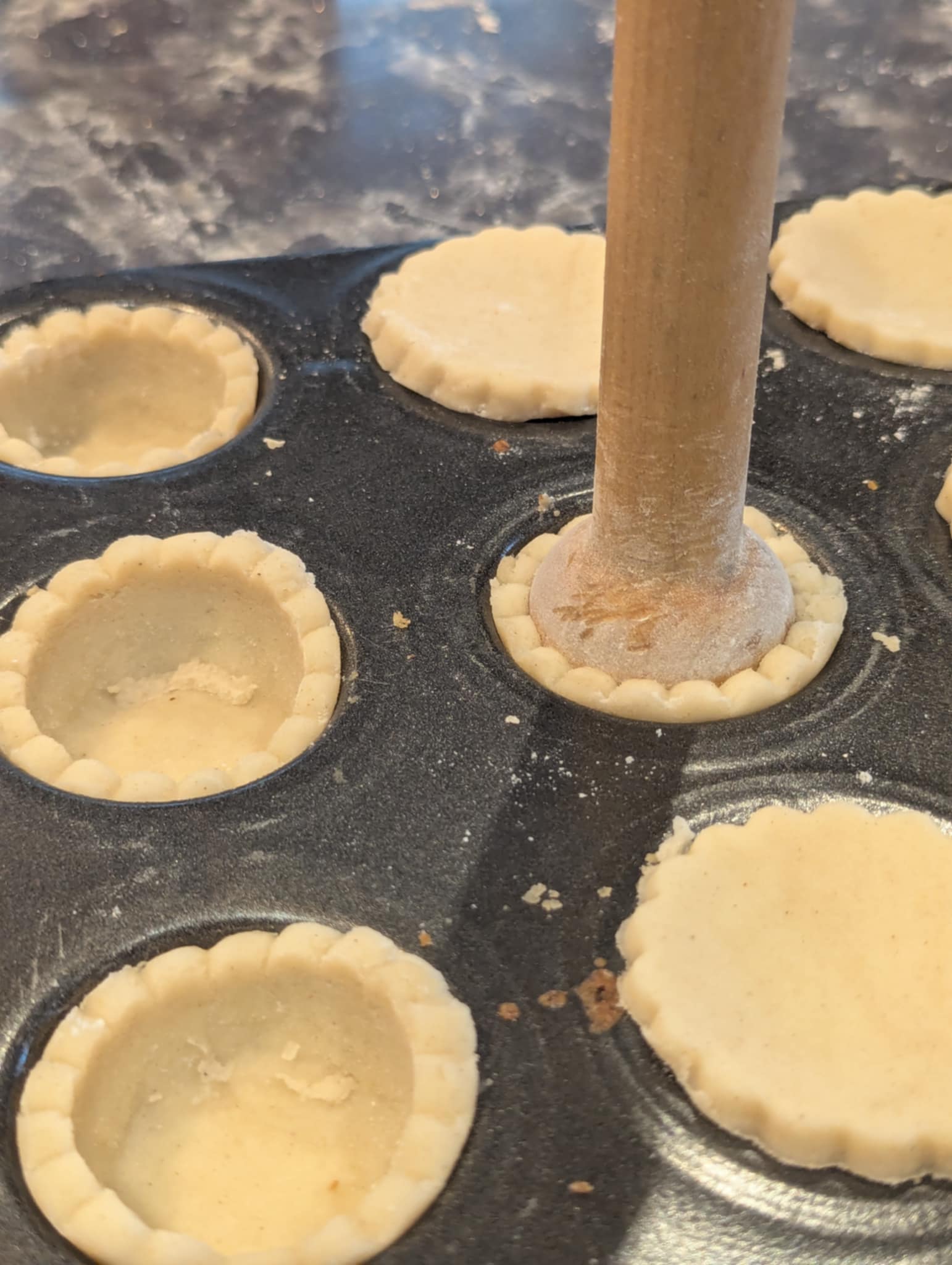 Using a wooden tart tamper to press cream cheese dough into mini muffin pan for pecan tassies