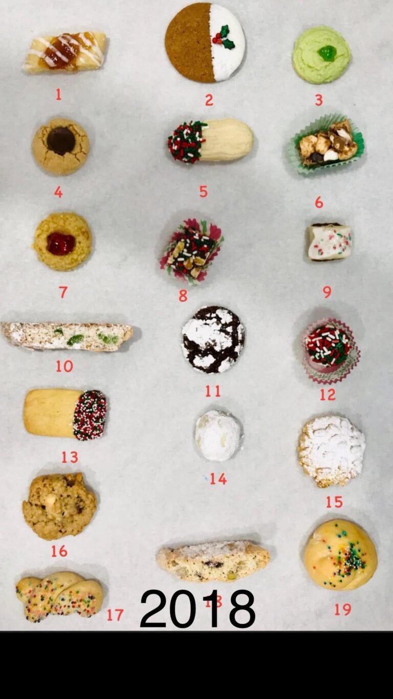 Top-down view of 19 different Christmas cookies laid out on white parchment paper, numbered 1 through 19 for a cookie box guide.