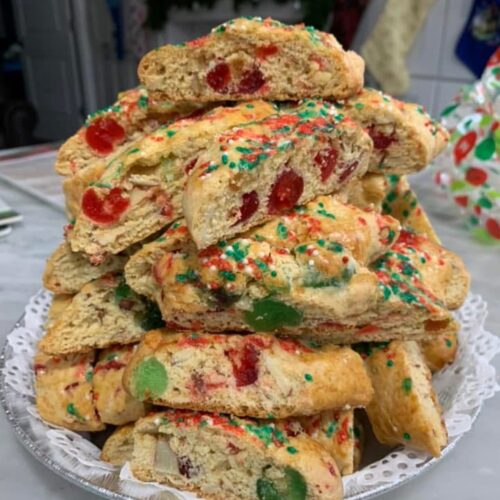 A tall stack of golden brown Cherry Almond Biscotti filled with red and green candied cherries.